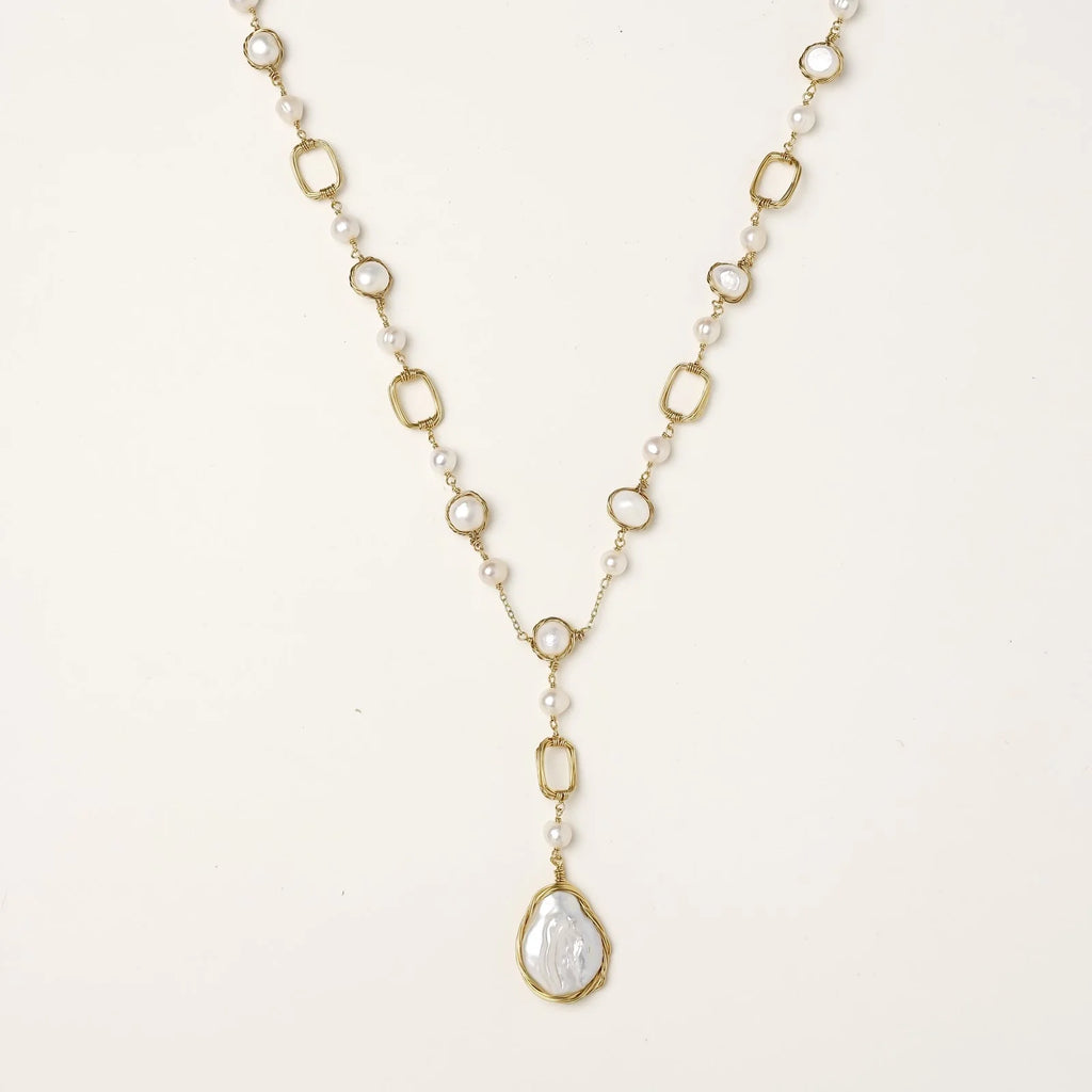 Y-shaped gold necklace with alternating geometric links, freshwater pearls, and baroque pearl pendant on cream background