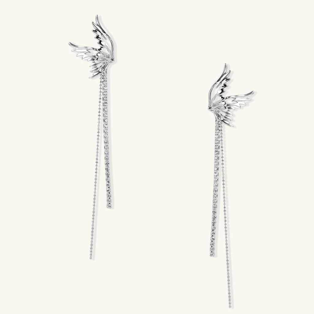 Pair of silver wing-shaped earrings with feather details and long sparkling crystal chain drops on cream background