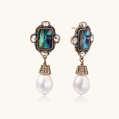 Ornate gold-plated earrings with iridescent abalone shell, crystals, blue stones, and white pearl drops on cream background.