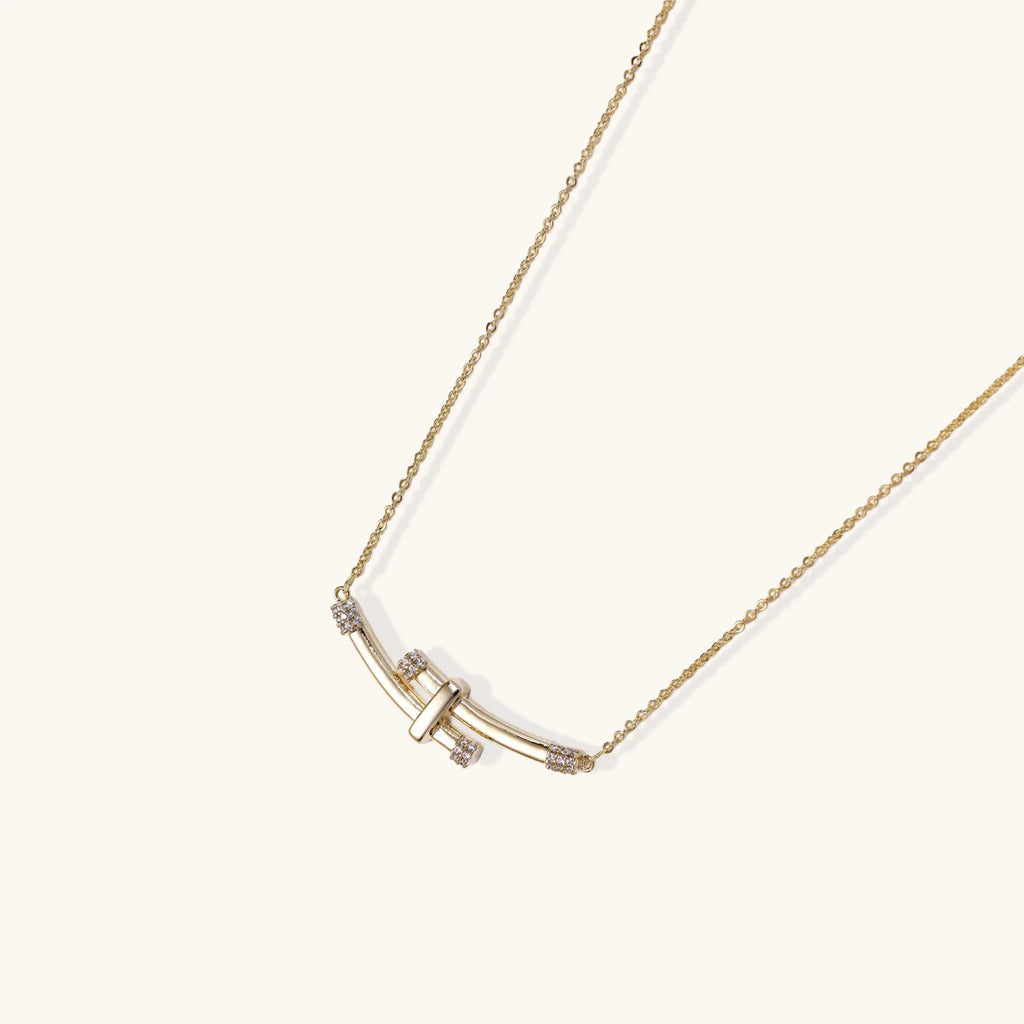 Gold-plated curved bar necklace with diamond accents on delicate chain against cream background