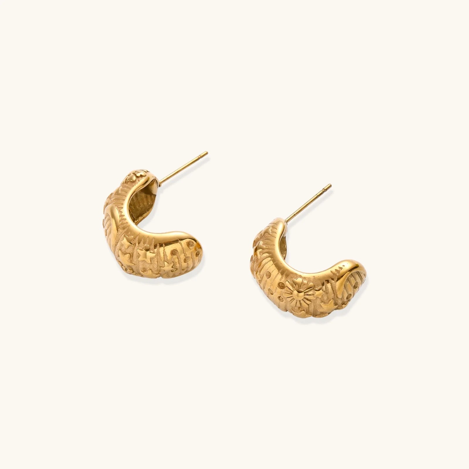 Gold-plated chunky hoop earrings with sun and star engravings on white background, showing detailed celestial pattern work.