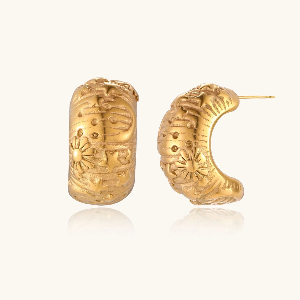 Gold-plated chunky hoop earrings with sun and star engravings on white background, showing detailed celestial pattern work.